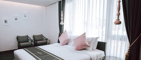 A hotel room with a large bed, two chairs, a small table, and a hanging light fixture.