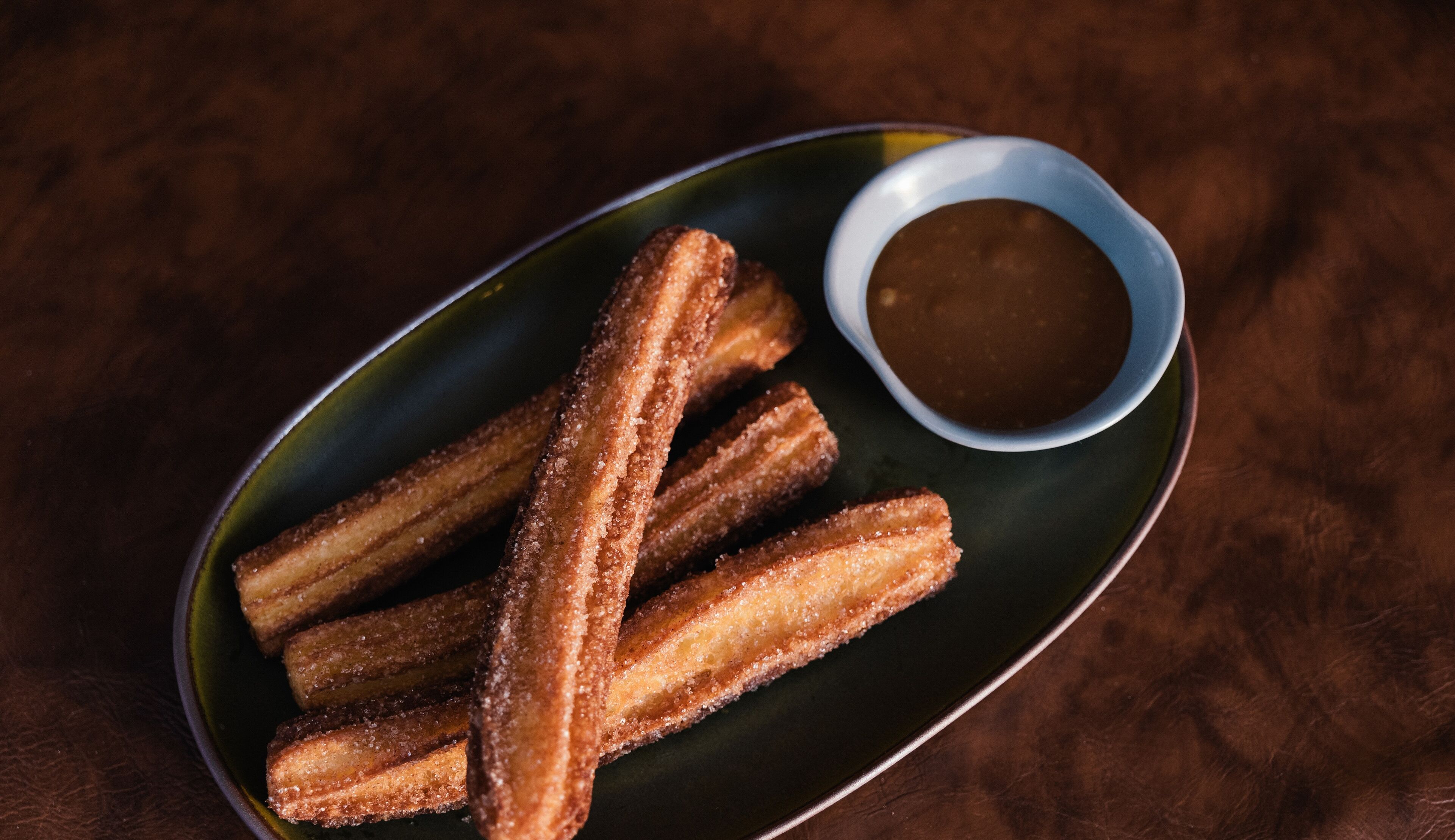 A plate of churros with a small bowl of dipping sauce.