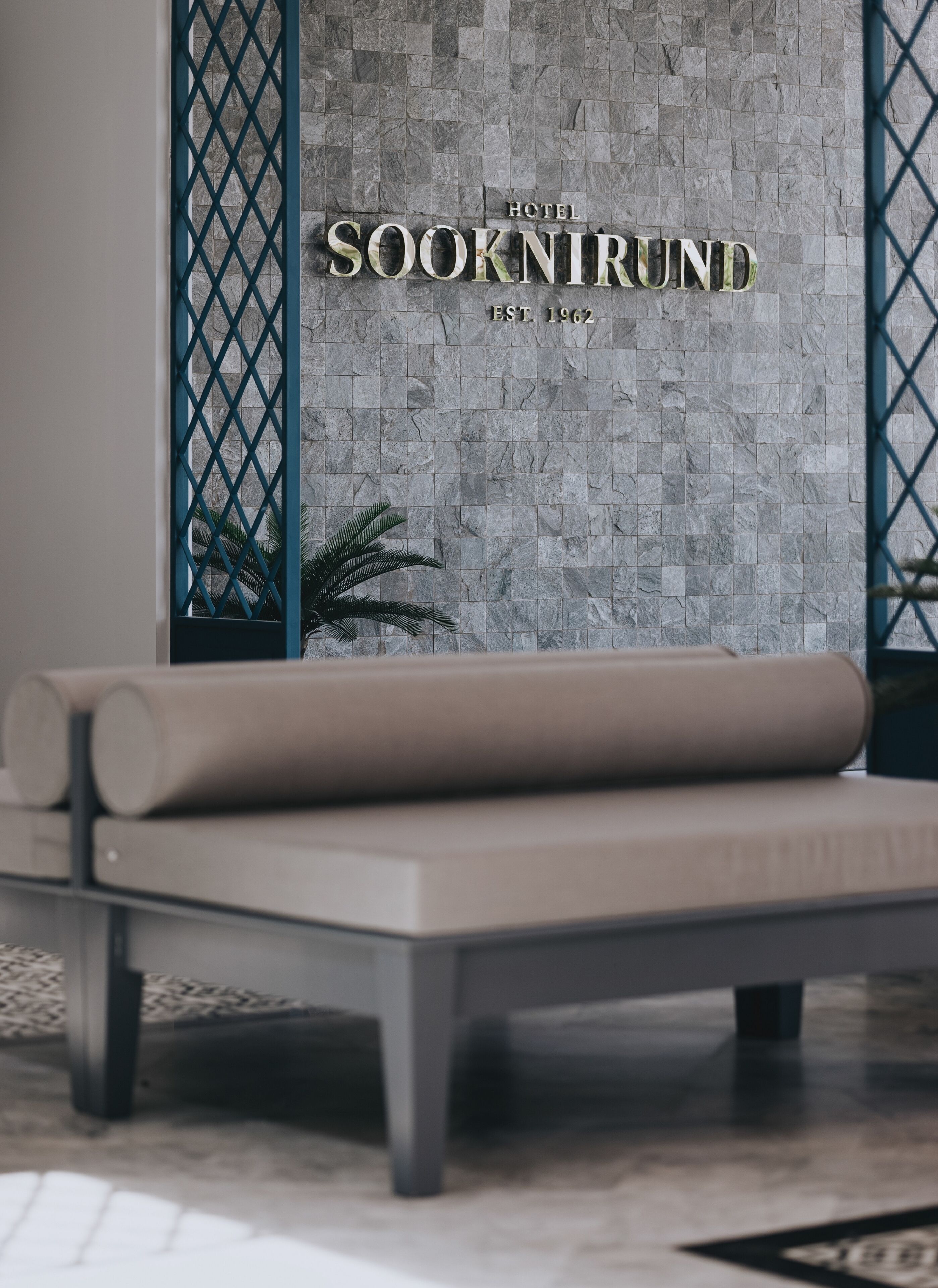 A modern hotel room with a stone wall and a bed with a beige mattress.