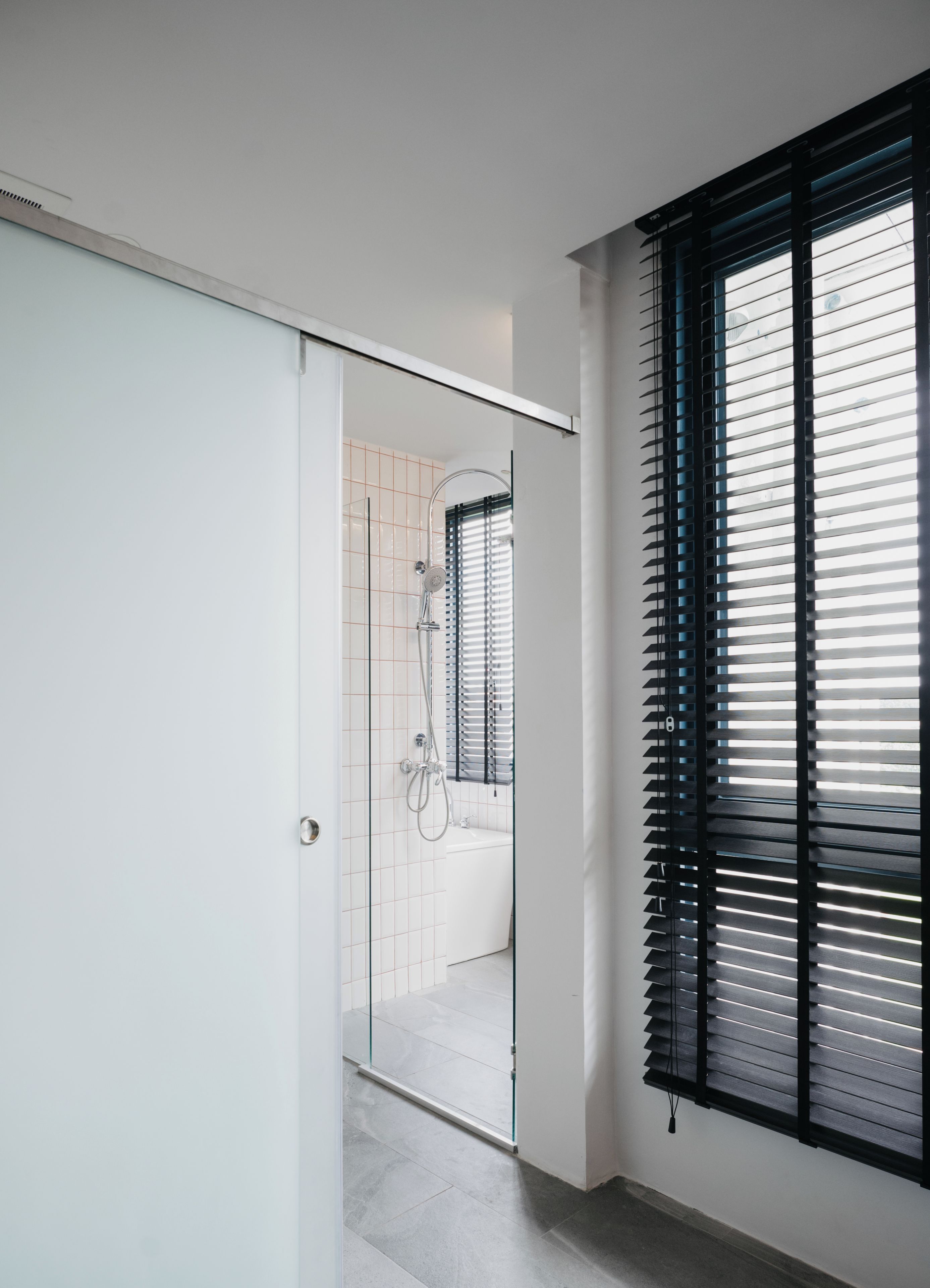 Ein modernes Badezimmer mit einer Duschkabine aus Glas, einer weißen Tür und einem Fenster mit schwarzen Jalousien.