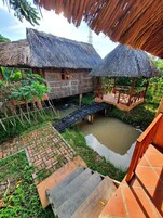 A rustic thatched-roof house with a small wooden bridge over a pond.