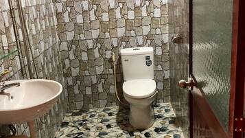 A bathroom with a stone mosaic wall, a white toilet, and a sink with a blue towel hanging on the wall.