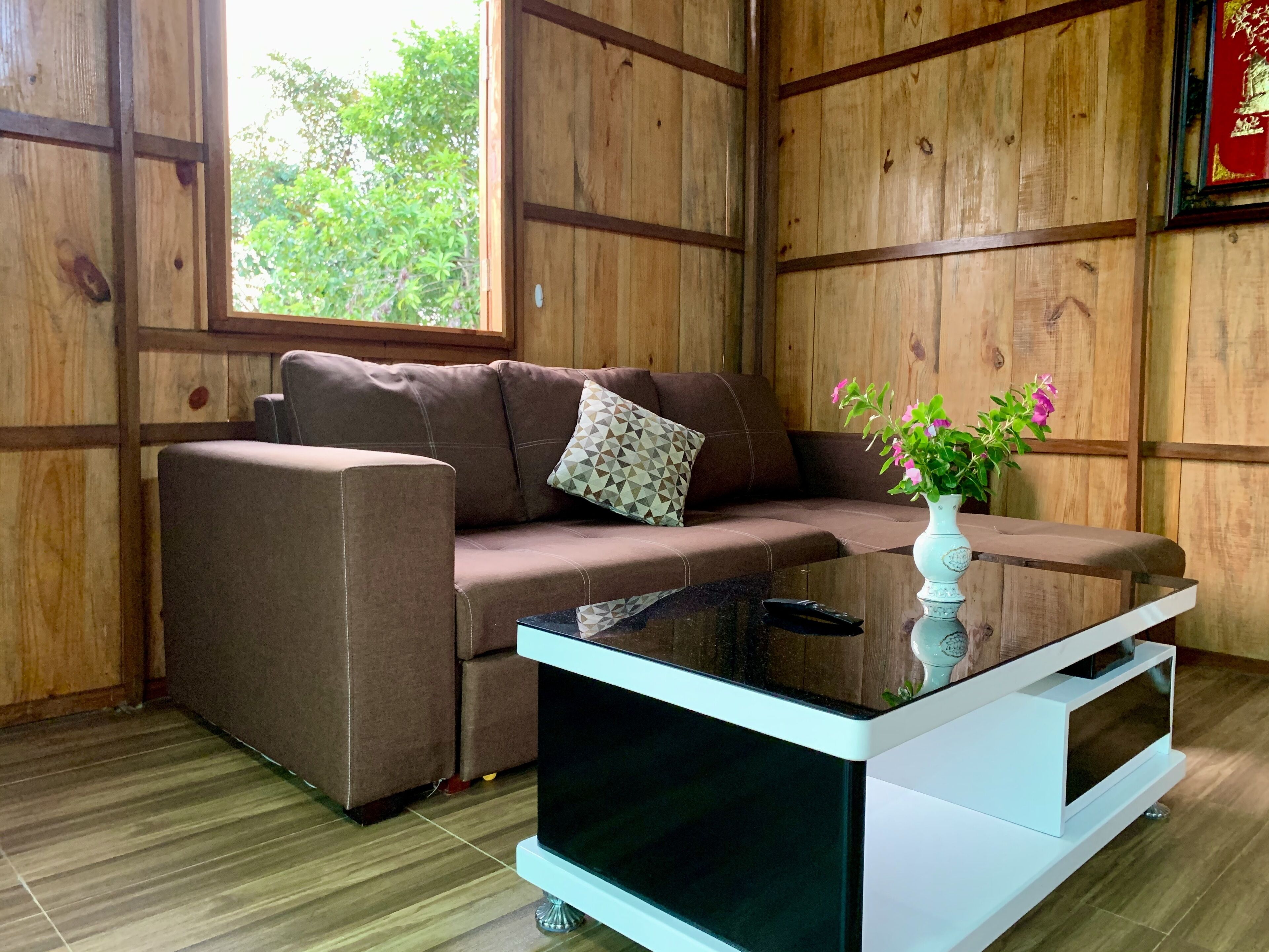 Una habitación acogedora con un sofá marrón, una mesita de centro de cristal y una pared de madera.