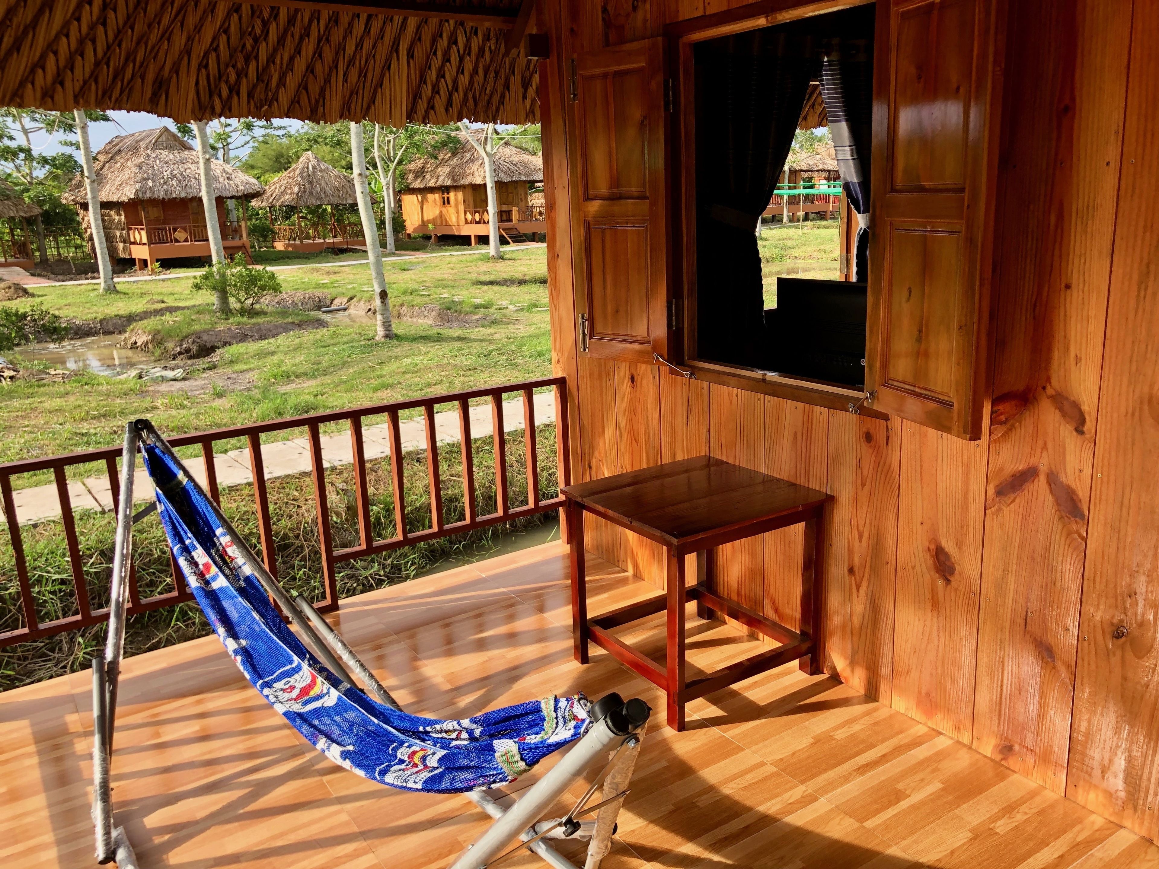 Eine Holzblockhütte mit einer Hängematte auf der Veranda, einem kleinen Tisch und Blick auf die Umgebung.