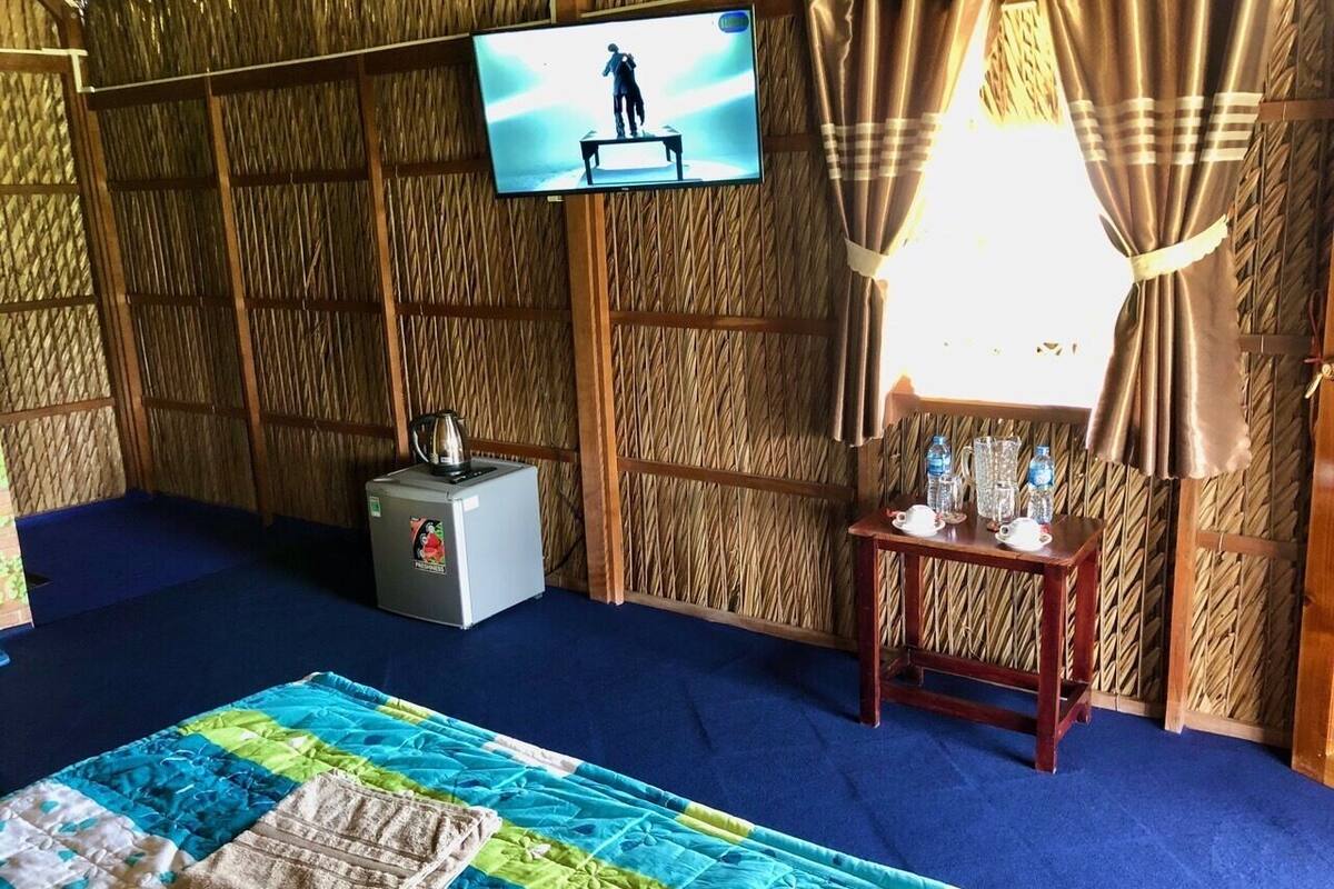 Habitació amb un llit, una televisió penjada a la paret, una taula petita amb ampolles d'aigua i una catifa blava.