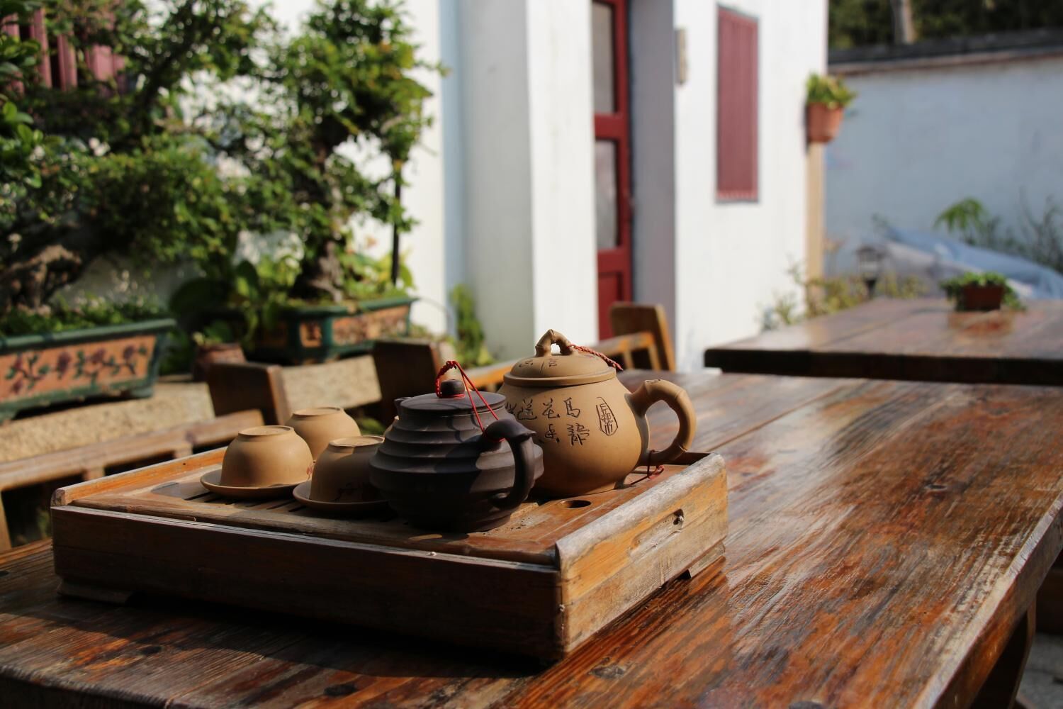 A wooden table with a tray holding various ceramic tea pots and cups.