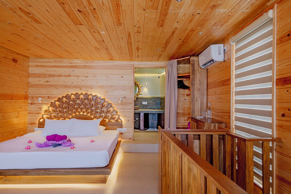 Een slaapkamer in een houten chalet met een bed, een houten hoofdbord en een kleine kitchenette.
