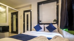 A hotel room with a bed, a bedside table, a mirror, and a window with curtains. - Hotel Satyug Inn (Ujjain)