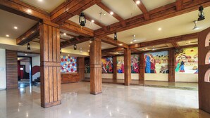 A spacious lobby with high wooden beams, polished tile flooring, and colorful murals on the walls. - Hotel Satyug Inn (Ujjain)
