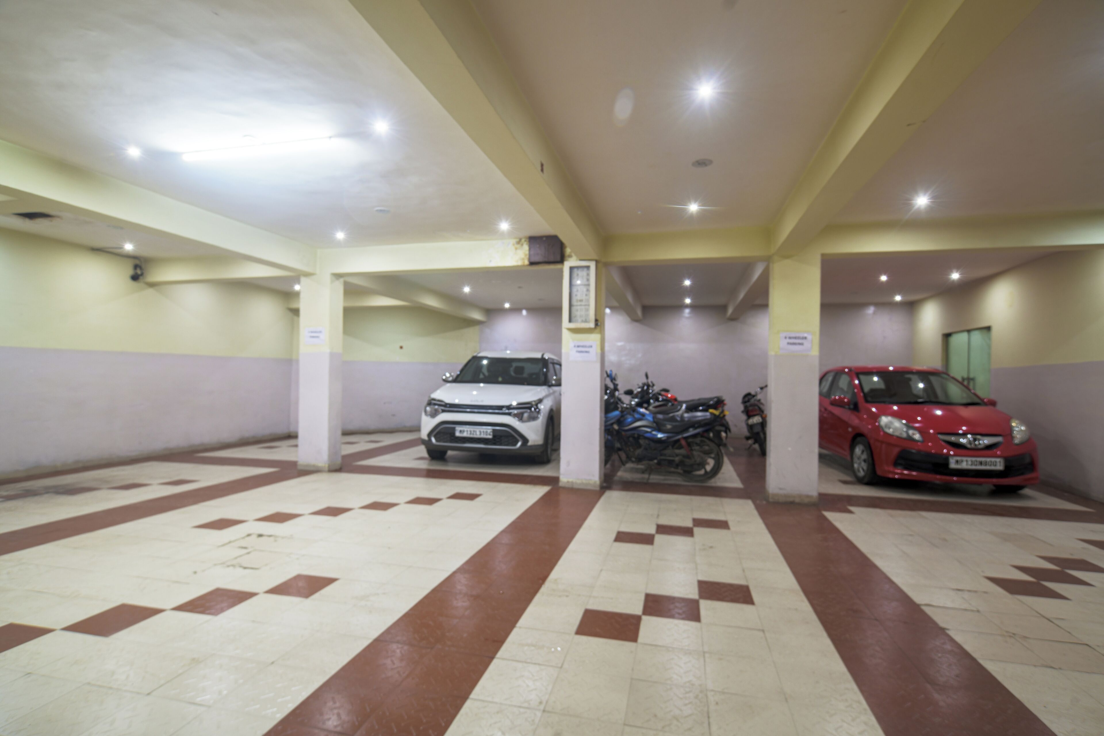 A parking garage with two cars and a motorcycle parked.