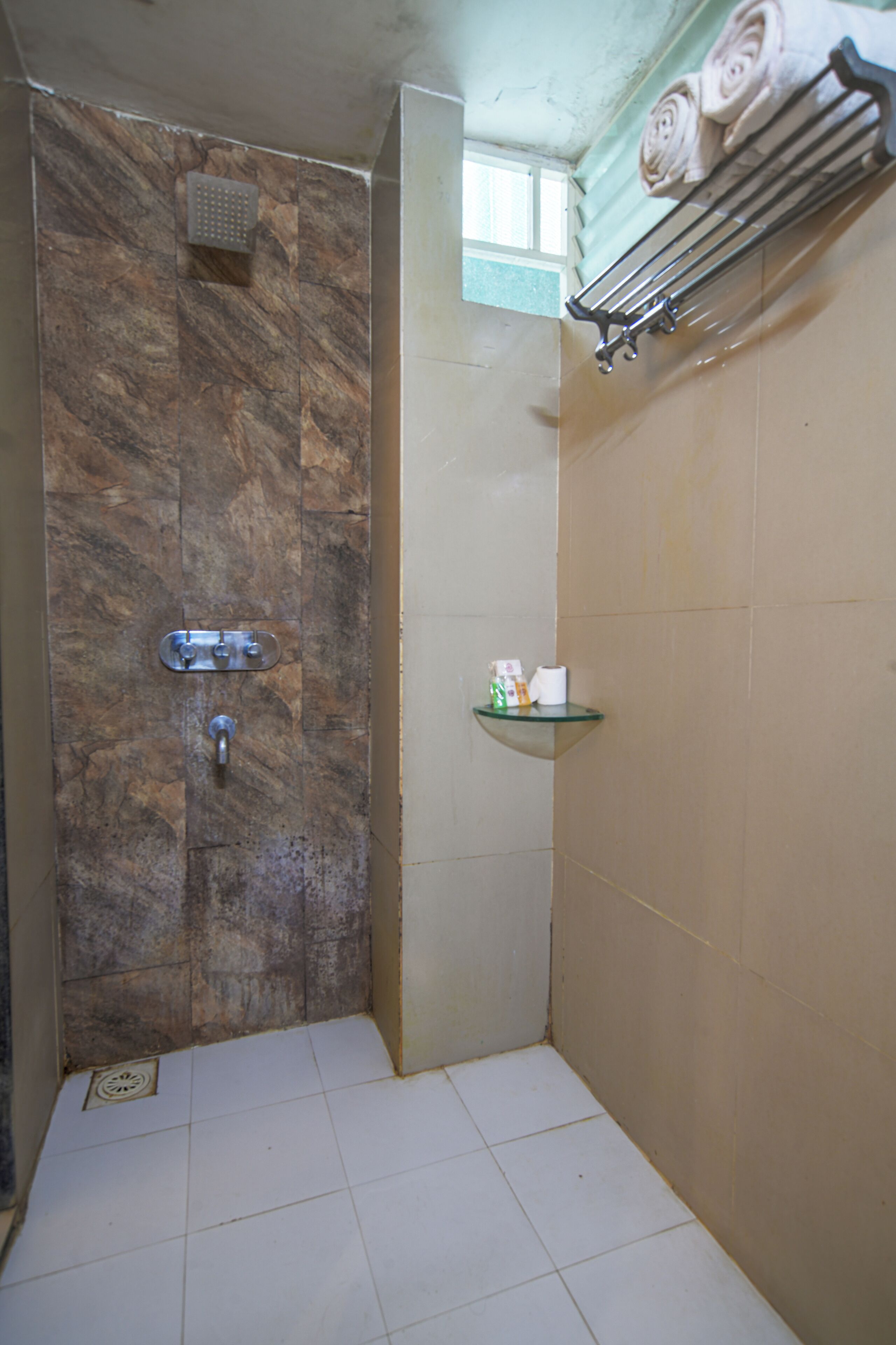 Un baño con ducha, repisa de vidrio con artículos de aseo y un perchero para toallas.