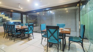 A modern dining area with a glass partition, blue chairs, and a wooden table. - Hotel Satyug Inn (Ujjain)