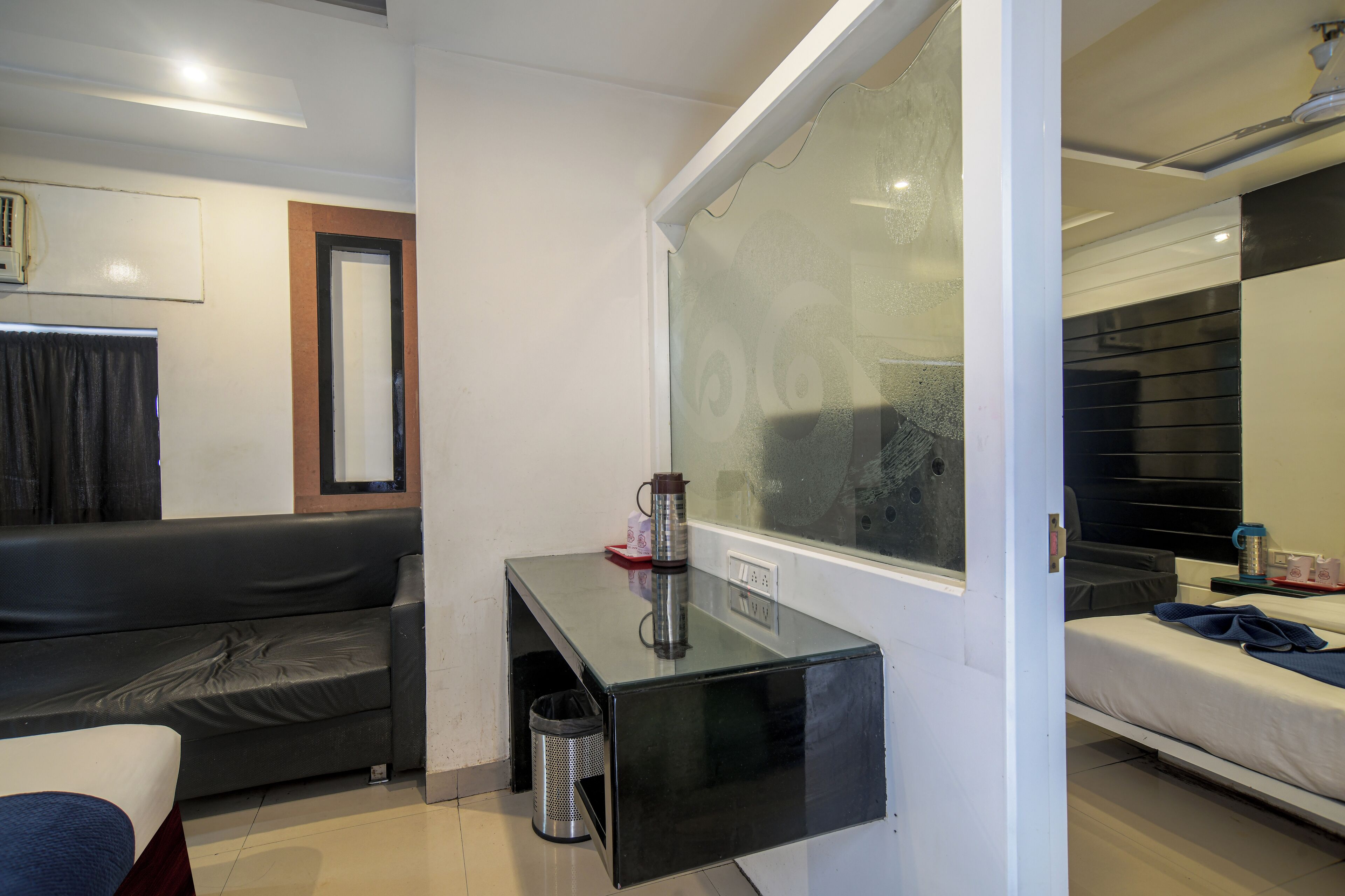 A modern hotel room with a glass partition, a sofa, a small table with a kettle, and a bed.
