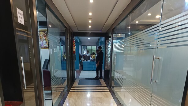 A hallway with glass doors and a marble floor leading to a reception area. - Hotel Satyug Inn (Ujjain)