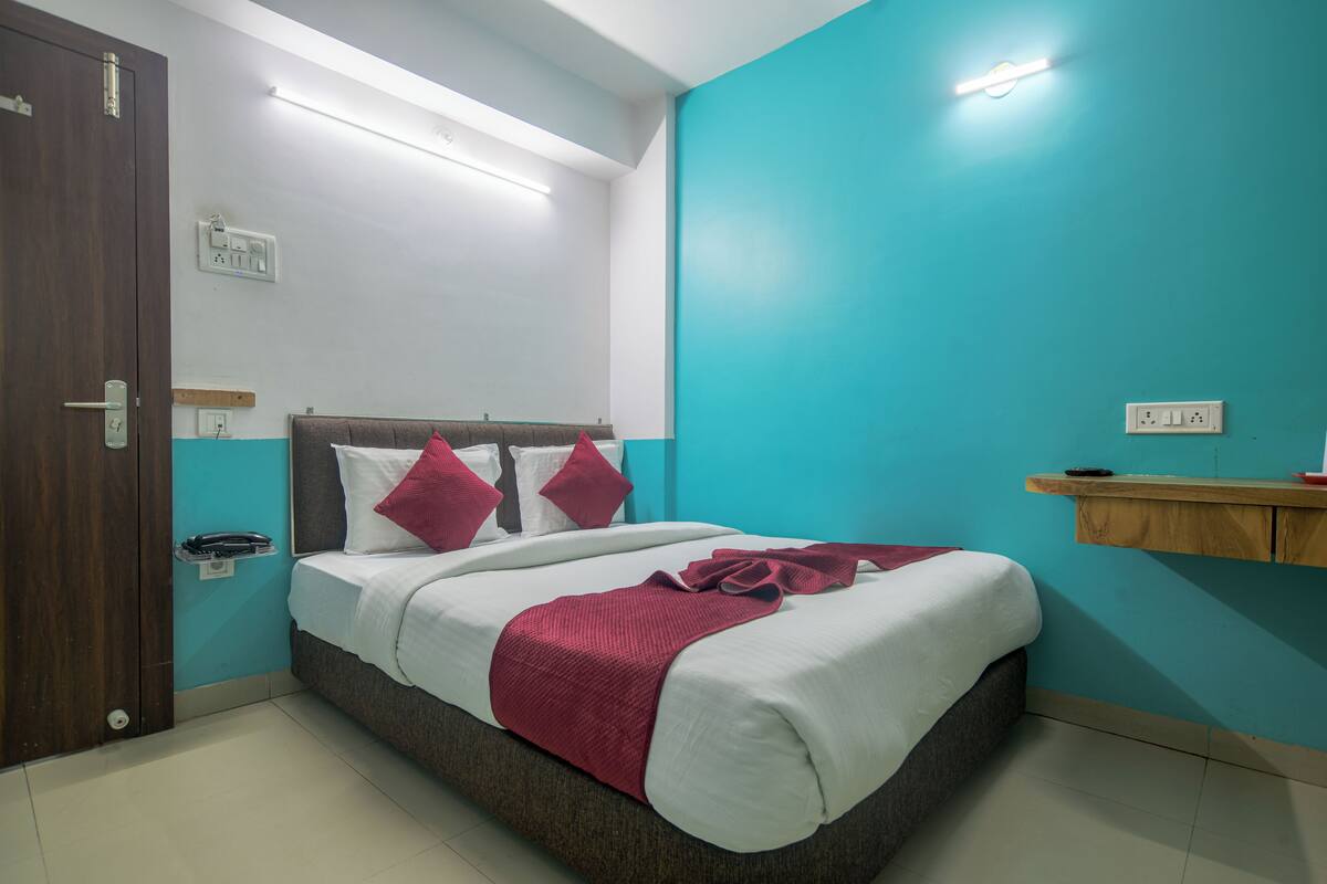 A bedroom with a bed, a wooden door, a light switch, and a wall socket.
