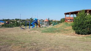 A playground with a blue slide and swings, a small gazebo, and a building with a red roof. - Saros Tepe Camping (Gallipoli)