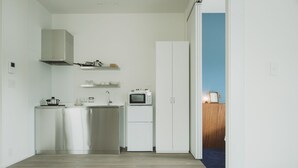 A compact kitchen with white cabinets, a microwave, and a stainless steel range hood. - Seacruise House Navio (Kamiamakusa)