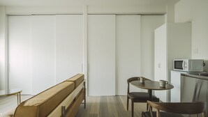 A modern, minimalist room with a wooden bench, a small round table with two chairs, and a microwave on a cabinet. - Seacruise House Navio (Kamiamakusa)