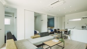 A modern, compact living space with a sofa, a small dining table, and a kitchenette. - Seacruise House Navio (Kamiamakusa)