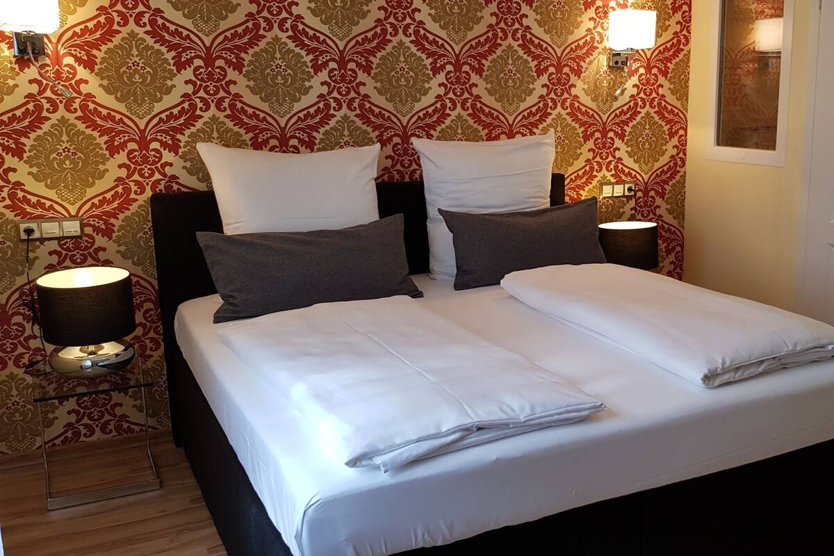 Un letto matrimoniale rifatto con lenzuola bianche, due abat-jour e carta da parati decorata.