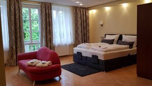 A bedroom with a bed, a red armchair, and a window with curtains. - Hotel Villa Lalee (Dresden)