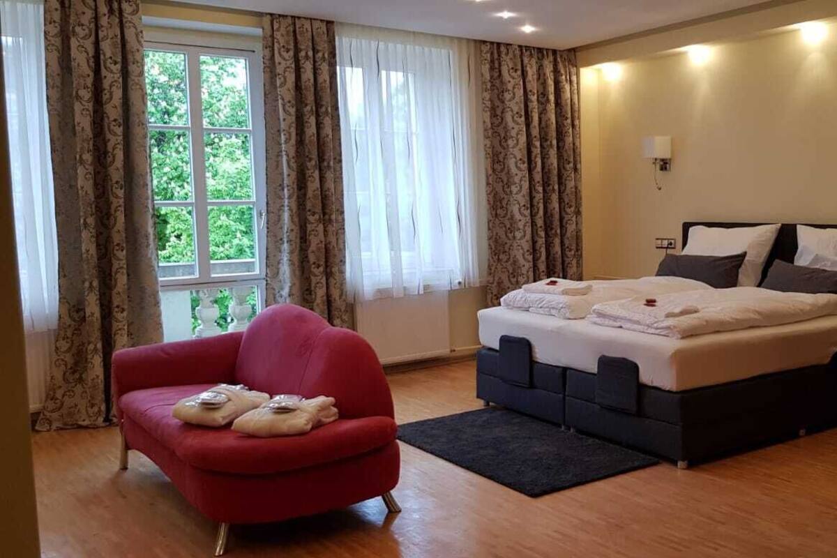 Una camera da letto con un letto, una poltrona rossa e una finestra con tende.