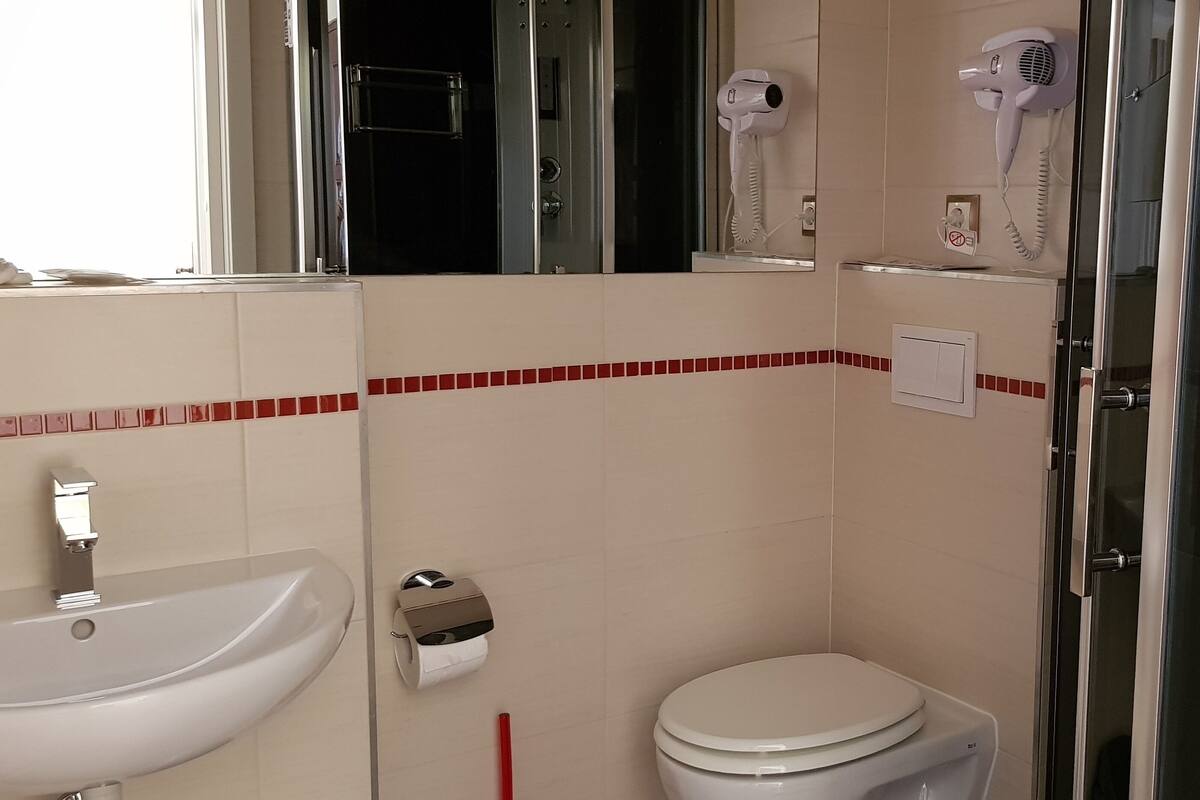Un bagno con lavandino, WC e due asciugacapelli fissati alla parete.