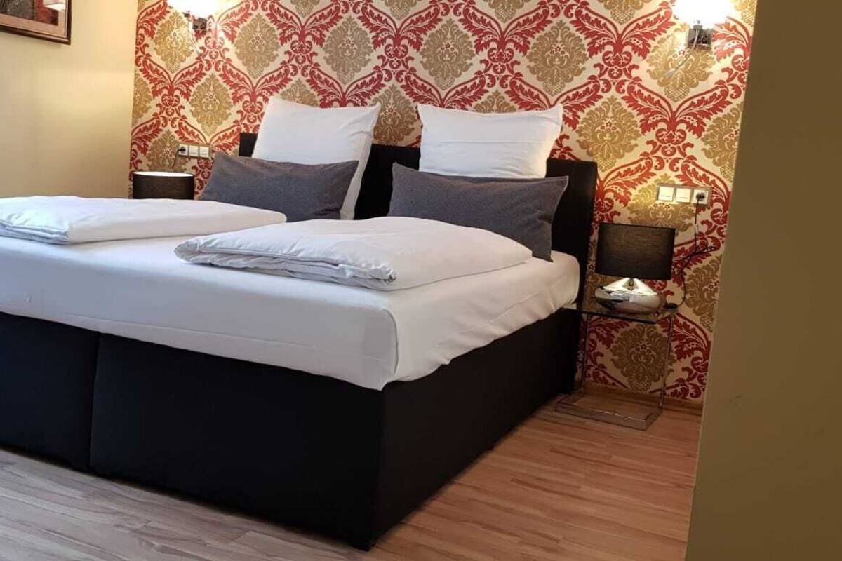 Un letto matrimoniale con lenzuola bianche, due comodini e carta da parati decorata.