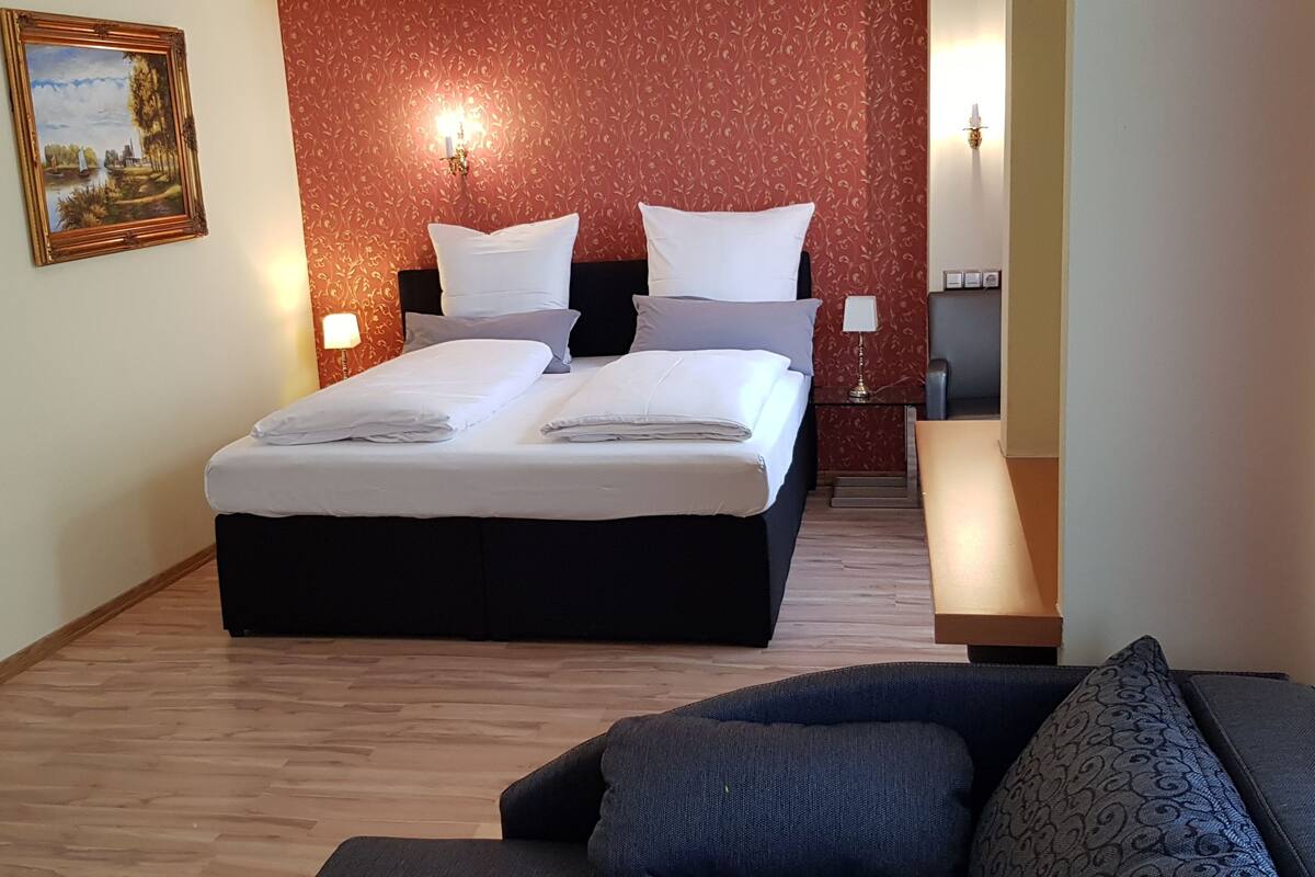 Una camera d'albergo con un letto grande, un divano, un quadro appeso e una parete decorata con un motivo rosso.