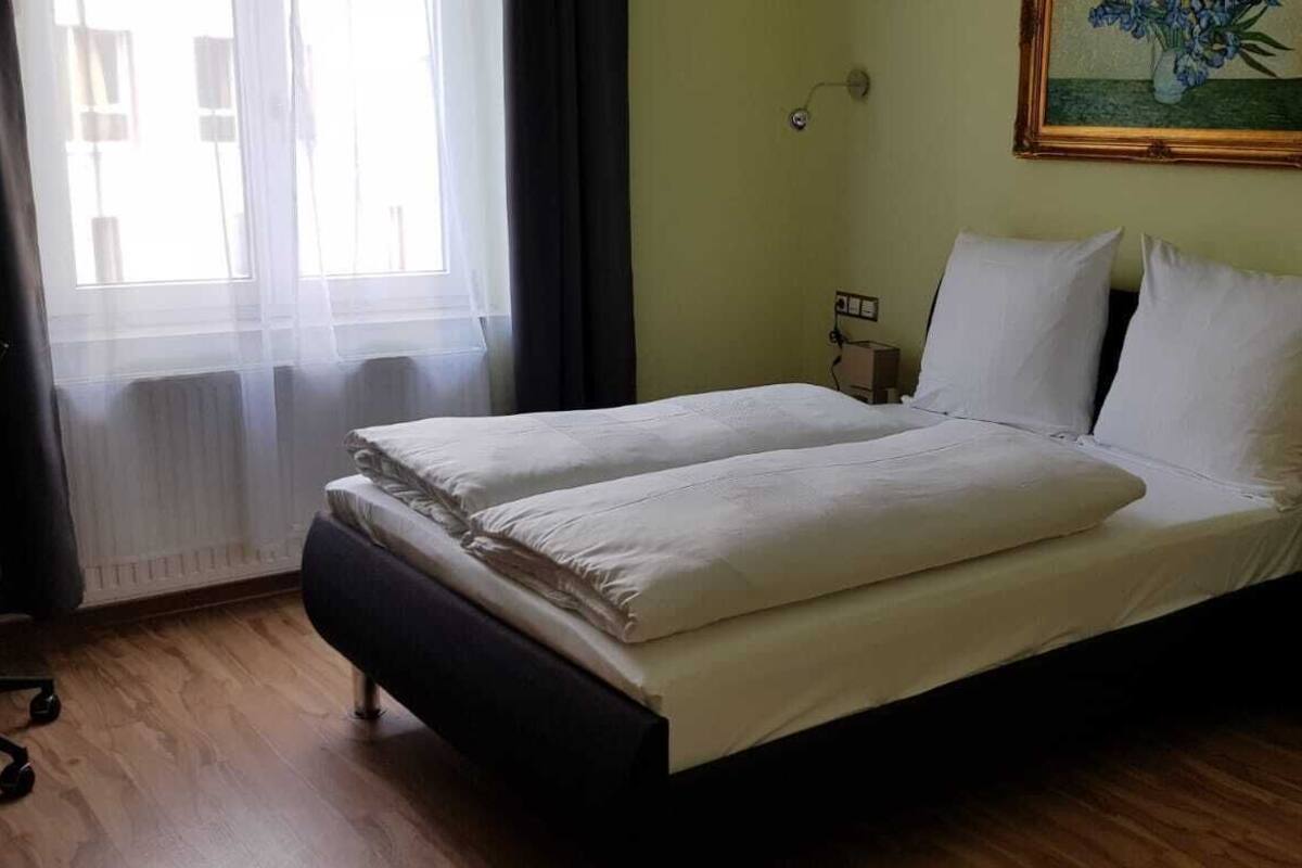 Un letto matrimoniale rifatto con cura in una stanza con pavimento in legno, un quadro al muro e una finestra con tende.