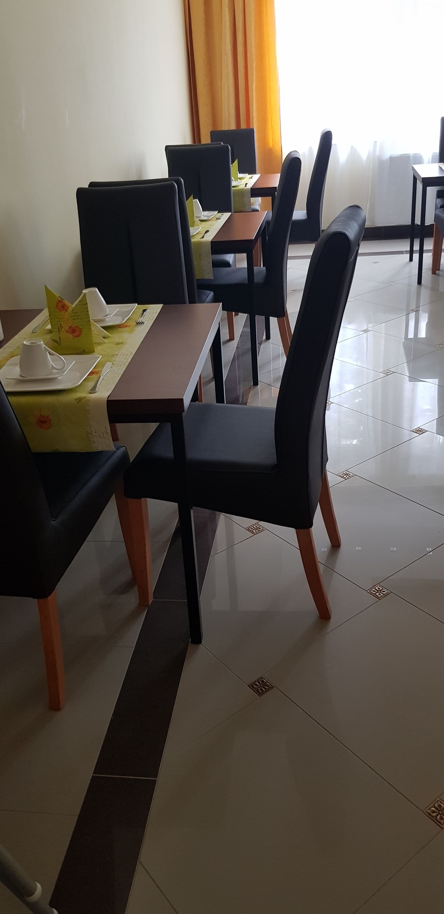 Un comedor con mesas dispuestas para cuatro, cada una con sillas negras y mantel verde.