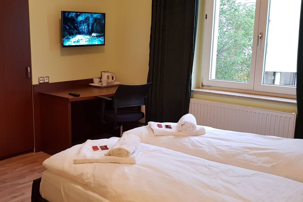 Camera d'albergo con un letto, una scrivania, una sedia, una TV e una finestra vista alberi.