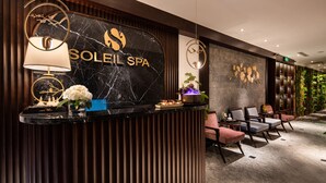 Ein Empfangsbereich mit einer Marmor-Theke, einem Schild mit der Aufschrift 'SOLEIL SPA' und einer Sitzecke mit Stühlen und einem kleinen Tisch.