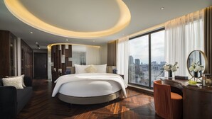 Ein modernes Hotelzimmer mit einem großen Bett, einem runden Schreibtisch und Blick auf die Stadt.