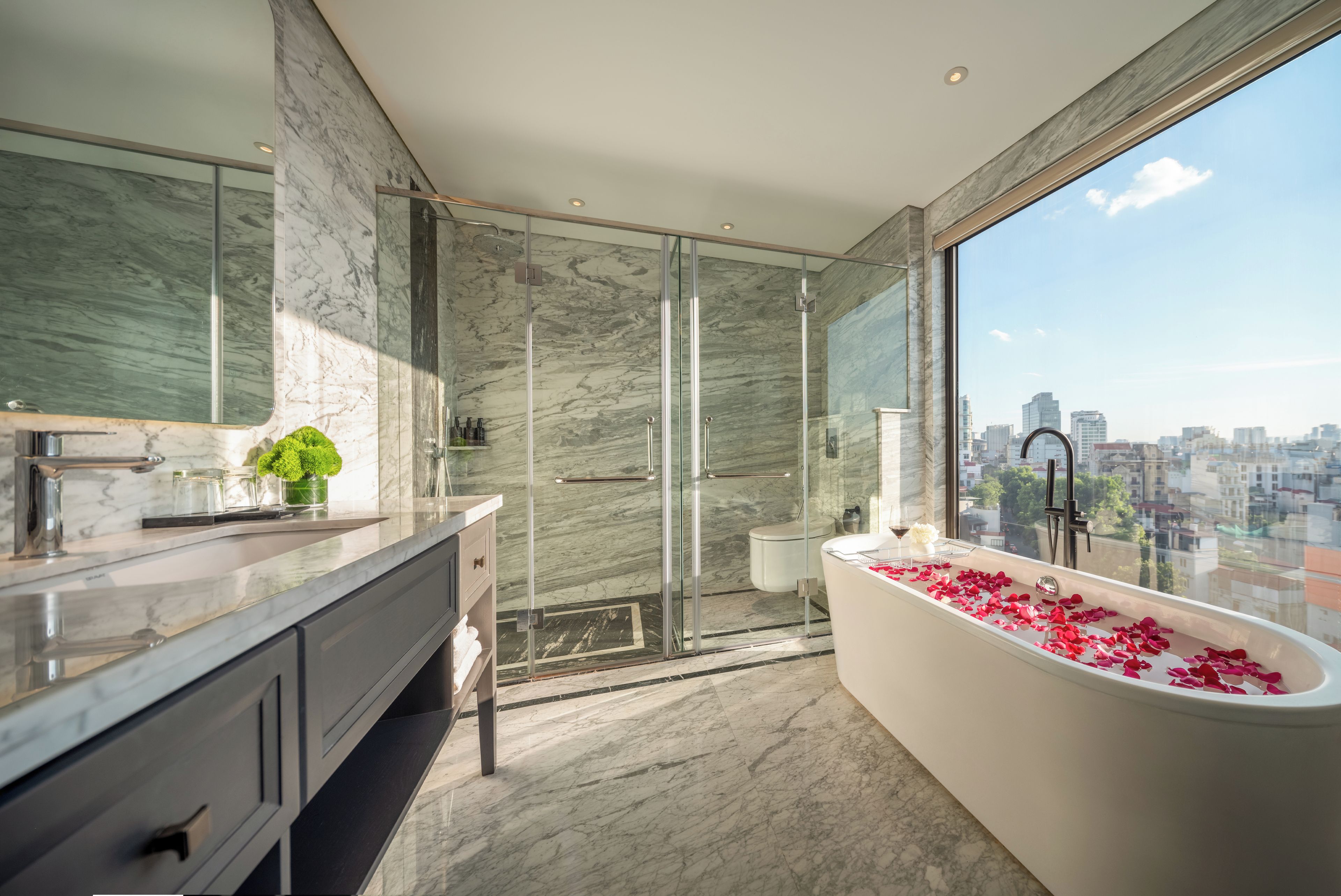 A modern bathroom with a large bathtub, a glass shower enclosure, and a city view.
