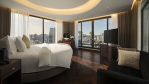 Ein modernes Hotelzimmer mit einem großen Bett, einer Couch, einem Fernseher und einem Balkon mit Blick auf die Stadt.