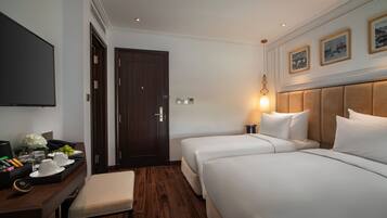 A hotel room with two beds, a desk with a tray of breakfast items, a flat-screen TV, and a wooden floor.