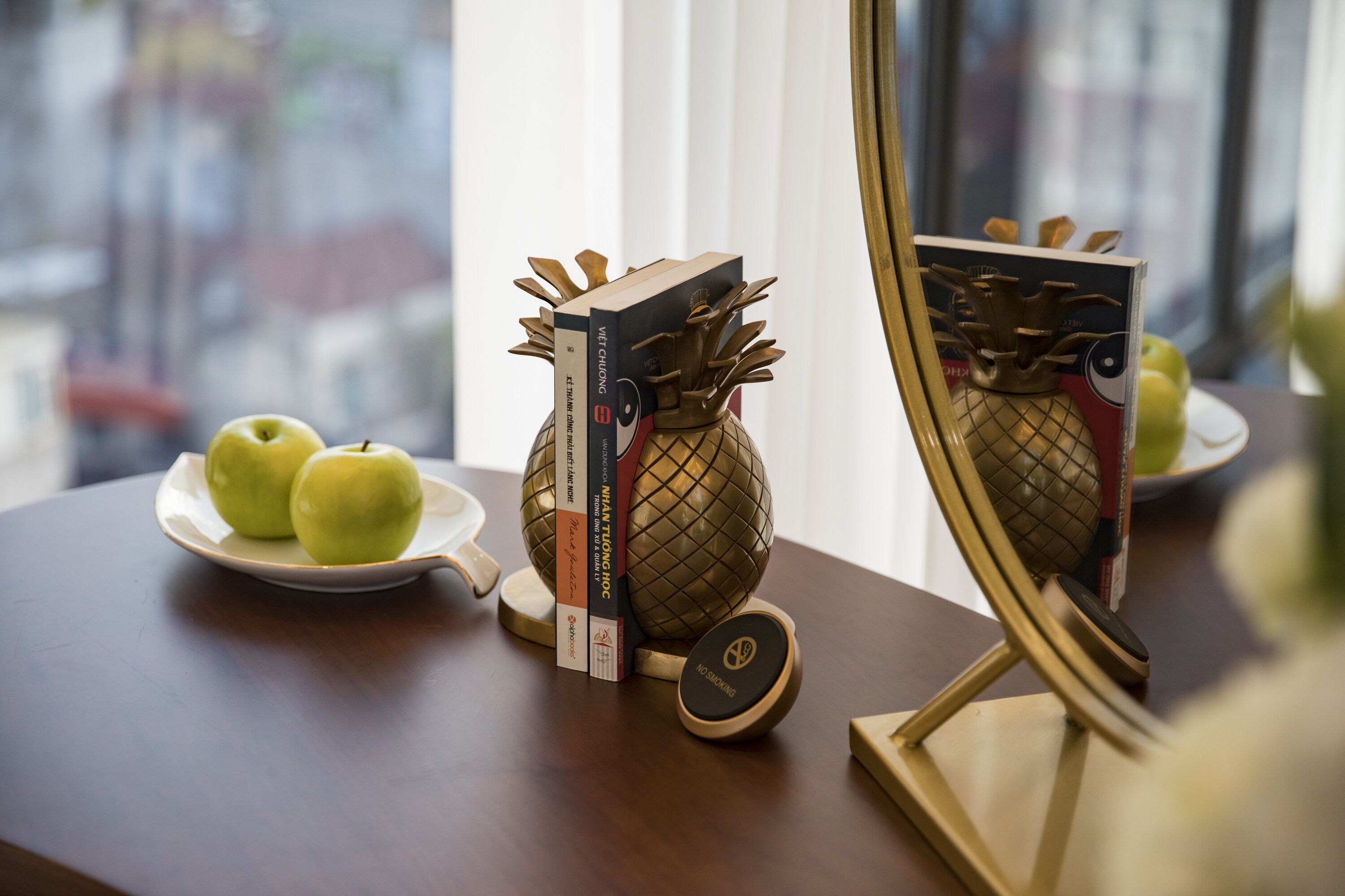 A wooden table with a decorative pineapple, books, and a plate with apples.
