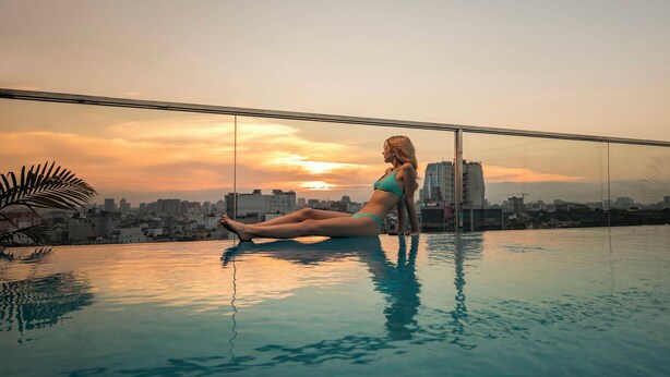 Eine Person sitzt an einem Infinity-Pool mit Blick auf die Stadtlandschaft.