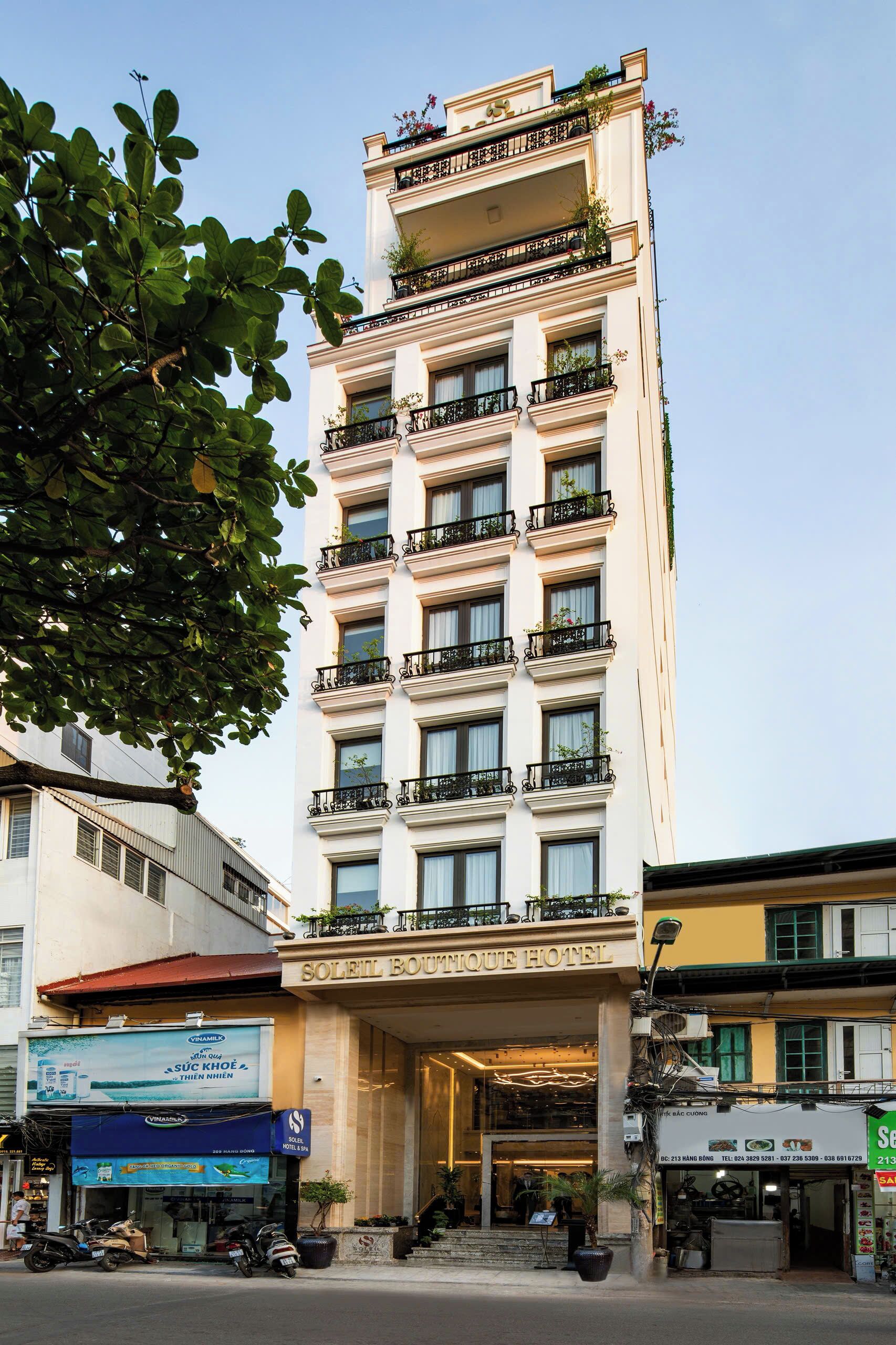 Un hotel de varios pisos con arquitectura clásica, que cuenta con balcones con plantas y una entrada destacada.