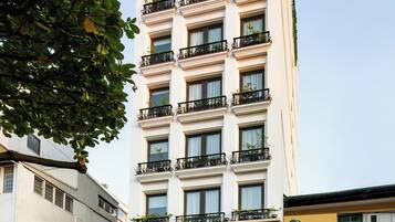 Un hotel de varios pisos con arquitectura clásica, que cuenta con balcones con plantas y una entrada destacada.