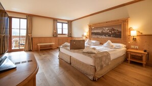 Une chambre d’hôtel avec un grand lit, un bureau, une chaise, une fenêtre avec des rideaux, un tableau au mur et une lampe.