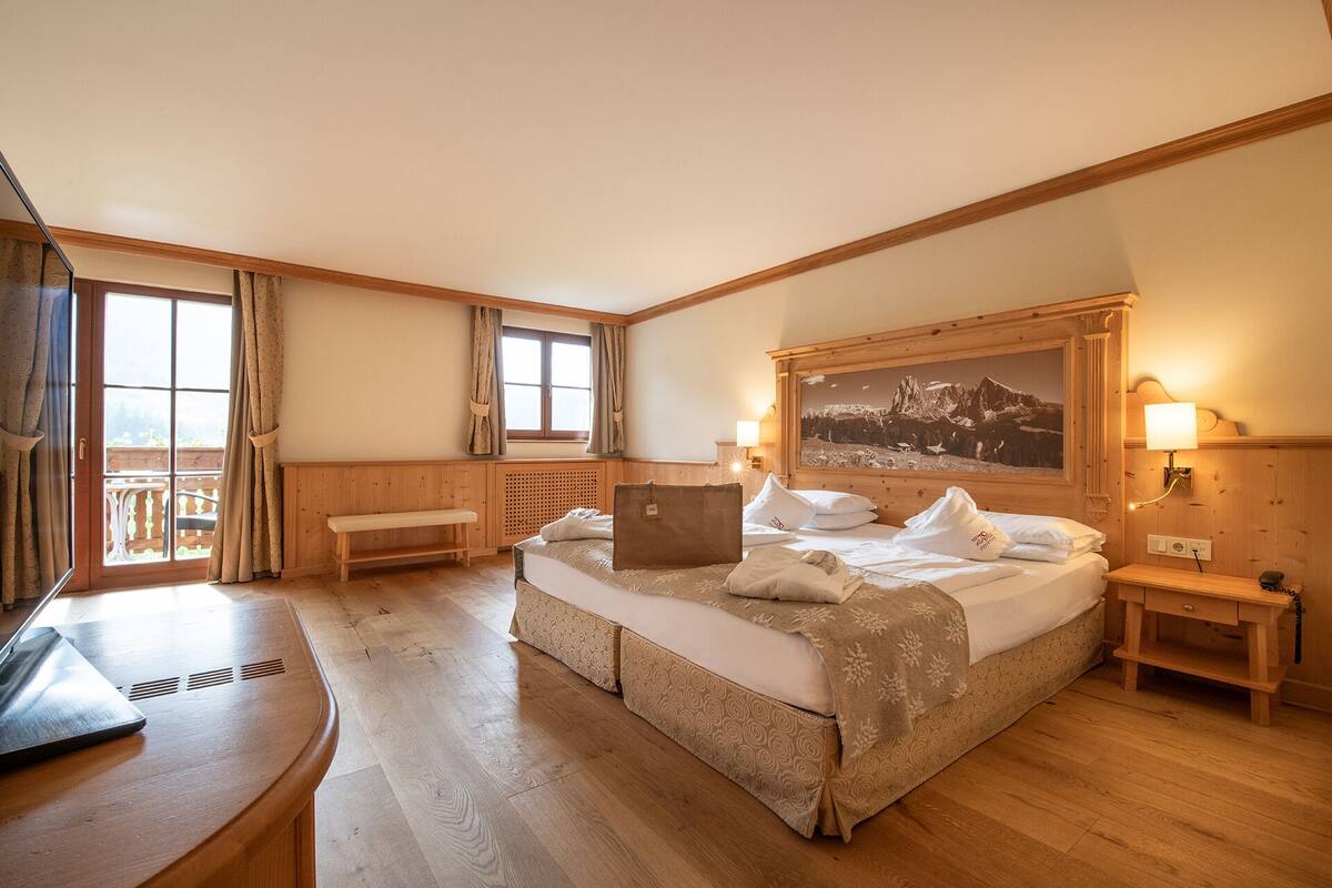 Une chambre d’hôtel avec un grand lit, un bureau, une chaise, une fenêtre avec des rideaux, un tableau au mur et une lampe.
