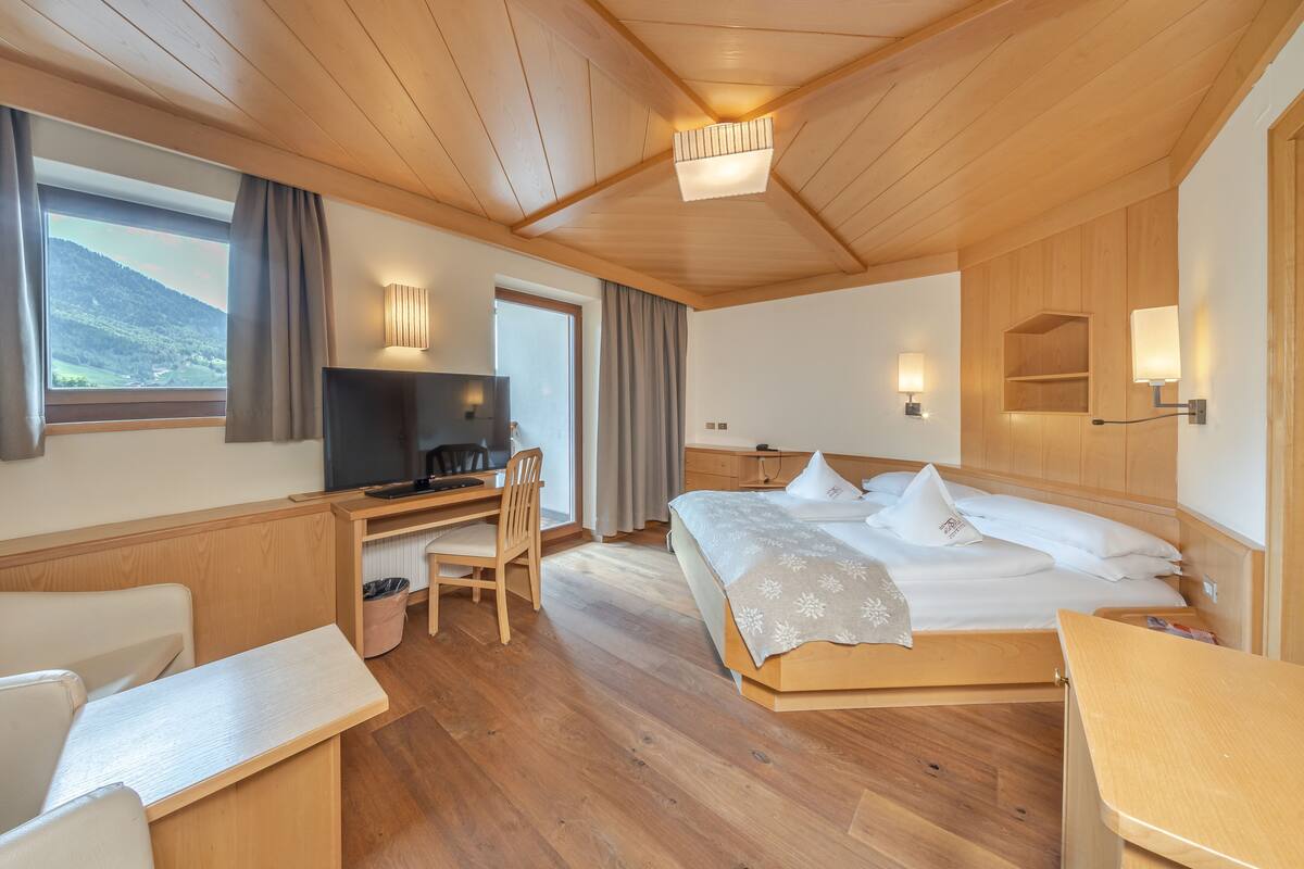 Une chambre d’hôtel avec un plafond en bois, un lit avec une literie blanche, un bureau avec une chaise, une télévision et une fenêtre donnant sur une montagne.