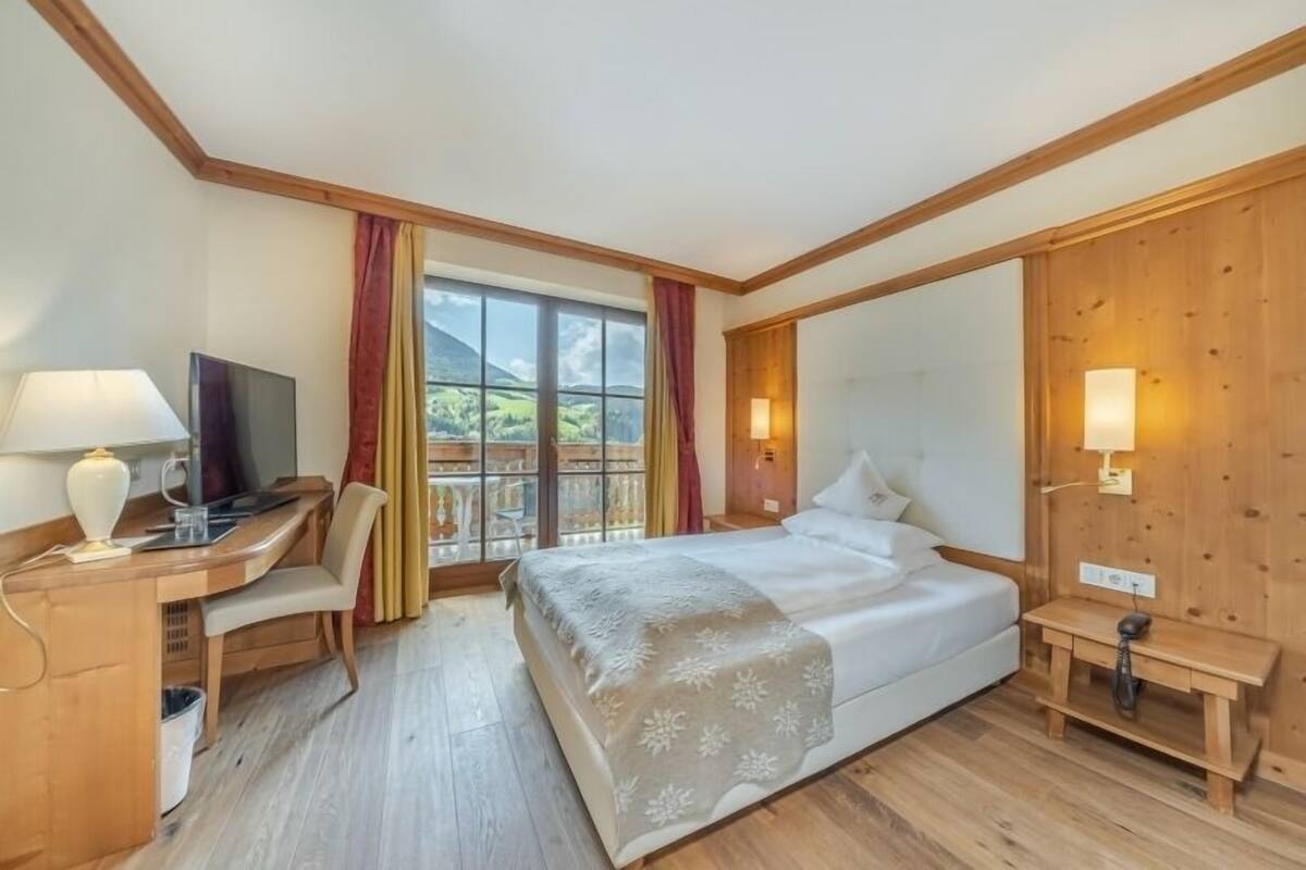 Une chambre d’hôtel équipée d’un lit, d’un bureau, d’une chaise, d’une télévision et d’un balcon avec des rideaux.
