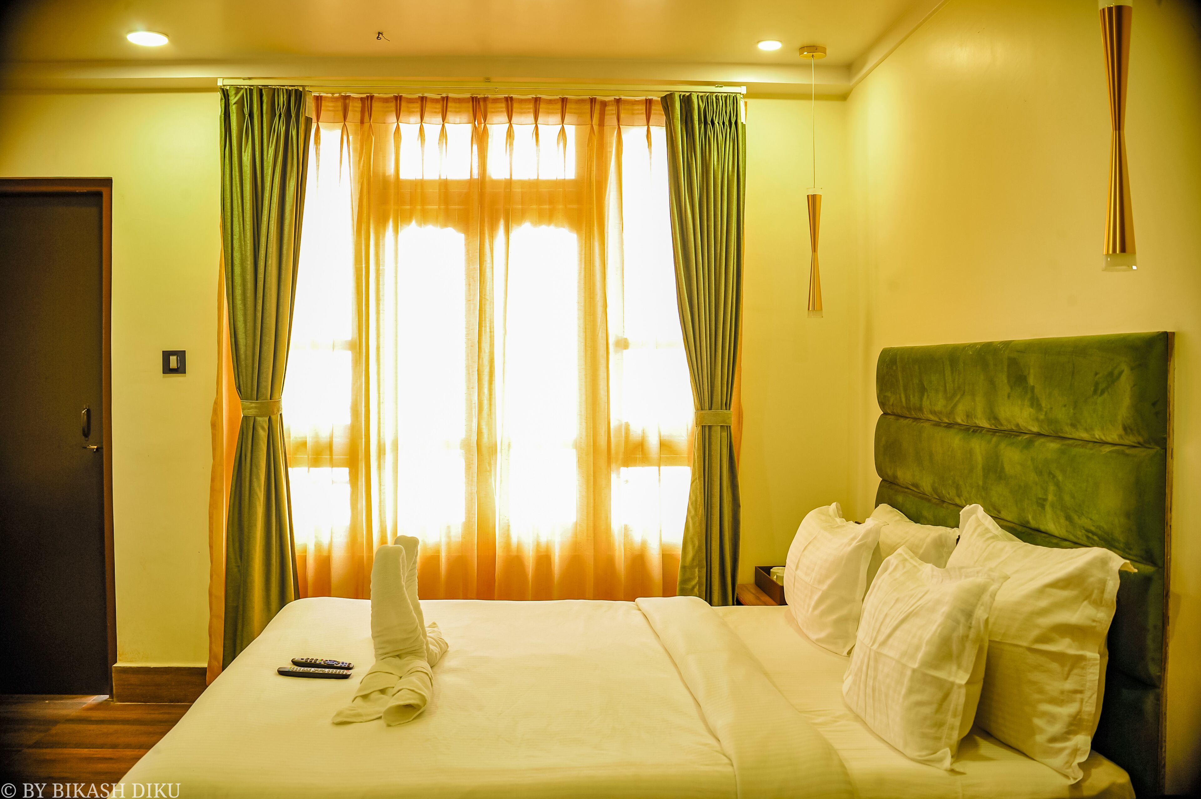 A hotel room with a bed, curtains, a headboard, and a remote control on the bed.