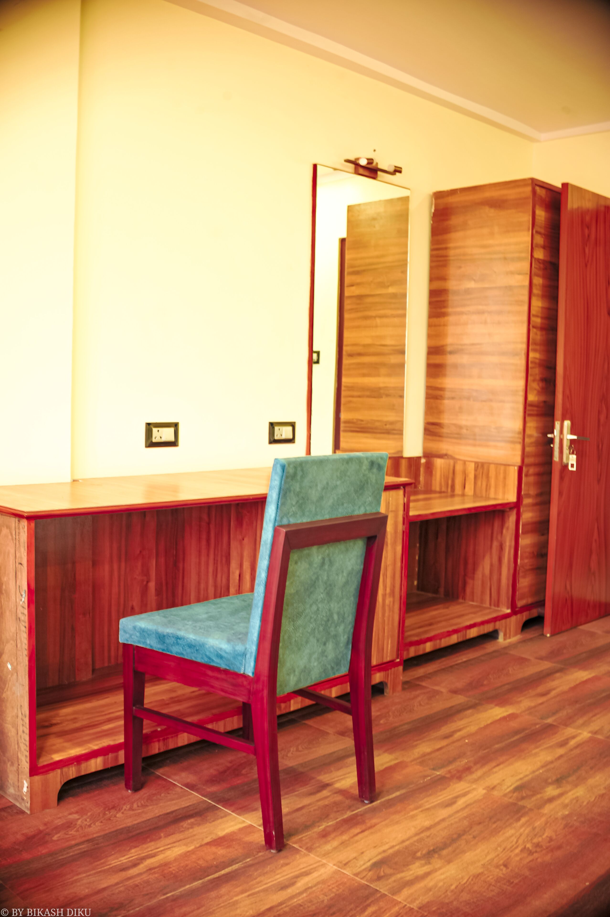A room with a wooden desk, a chair, a wardrobe, and a mirror.