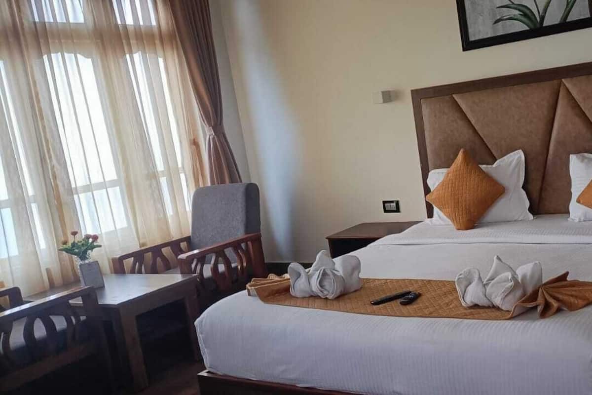 A hotel room with a large bed, a wooden nightstand, a desk with a chair, and a window with curtains.
