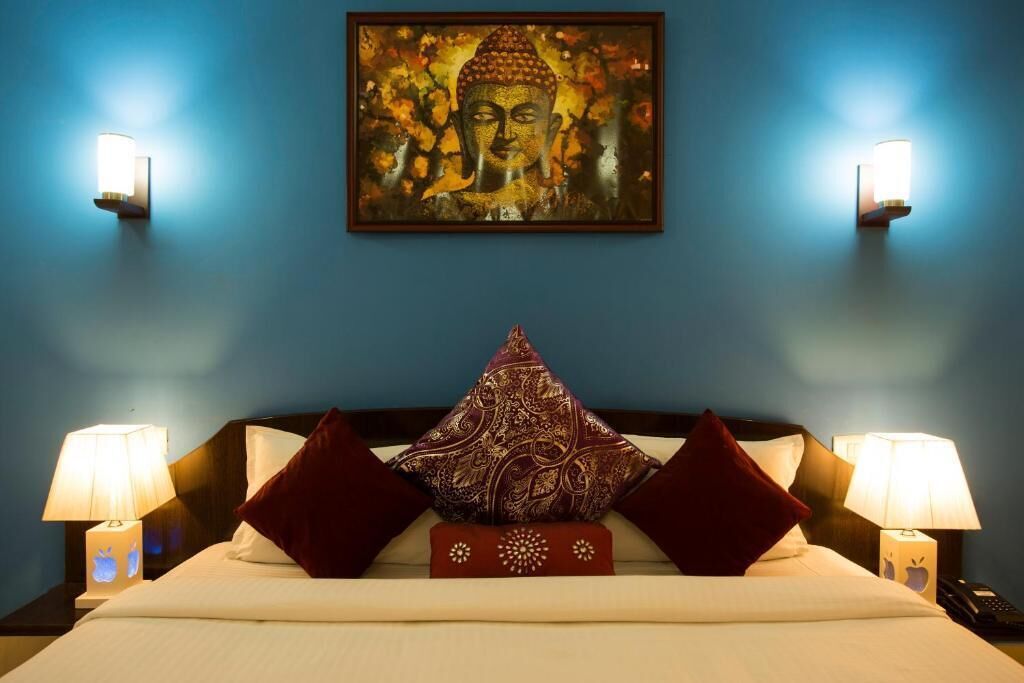 Habitación de hotel con cama, dos lámparas de pared, un cuadro enmarcado de Buda y almohadones decorativos.