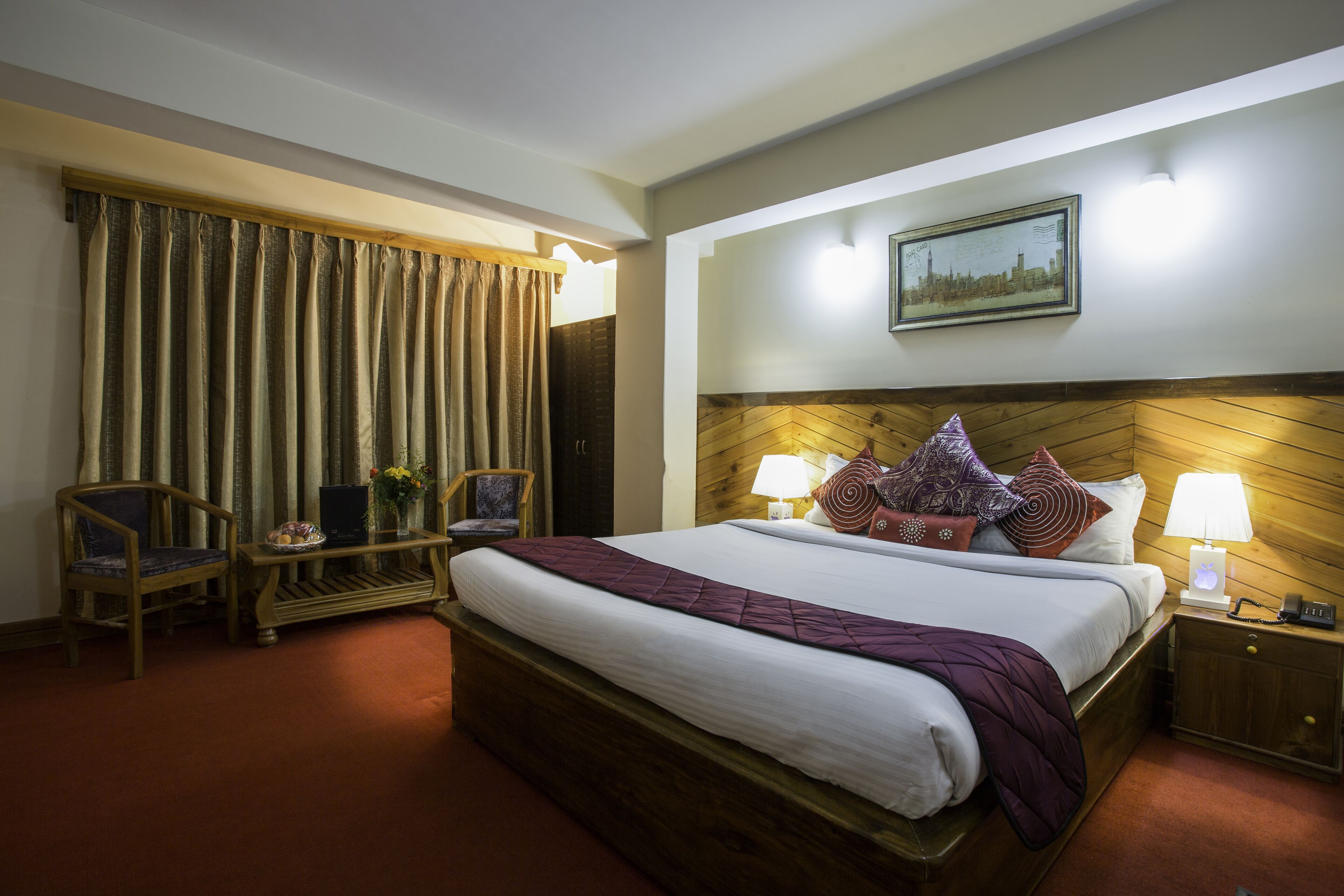 Ein Hotelzimmer mit einem großen Bett, zwei Nachttischen, einem Sessel, einem Schreibtisch und einem großen Fenster mit Vorhängen.